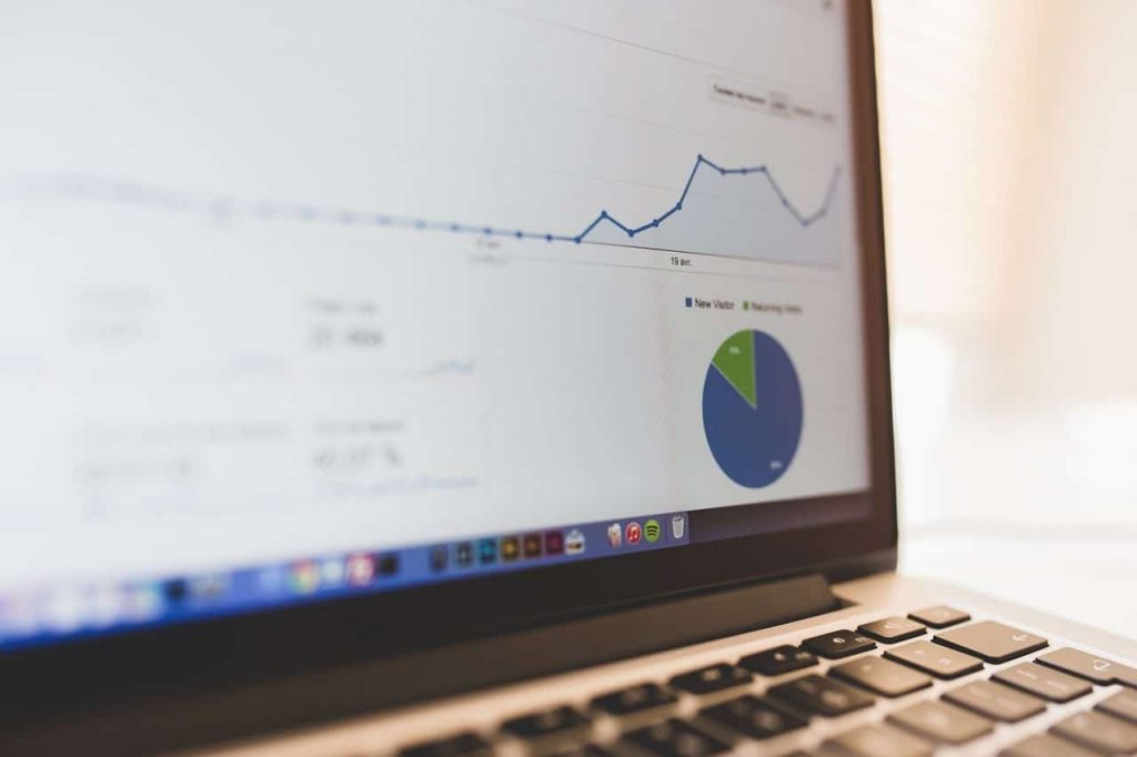 A graph with a rising trend and a pie chart are displayed on the screen of a laptop, suggesting data analysis or business statistics. The keyboard of the laptop can be seen partially in the lower right corner.